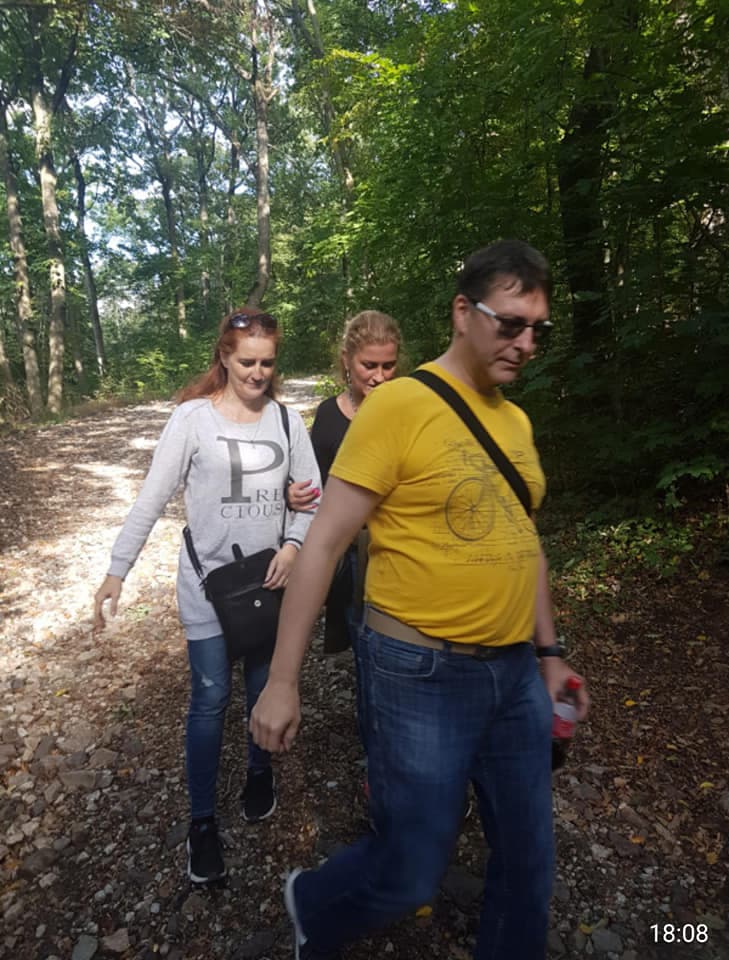 Skupina ľudí na kamenistej lesnej ceste, slnečné svetlo.